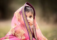 Professional photography by Nature's Child Photography: Infant child wrapped in a pink sari with gold embroidery looking toward the Baby girl in a pink tutu standing barefoot at the water’s edge, looking surprised as waves roll in during a beach child photography session- A portrait experience by Nature's Child Photography