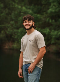 Senior portrait at Circle B Lake in Wilmer, Alabama — standing in jeans with a thumb in his
pocket, pond in the background.