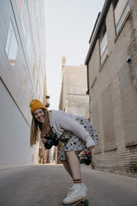 A person crouching in an alley as they laugh and hold a camera with one hand