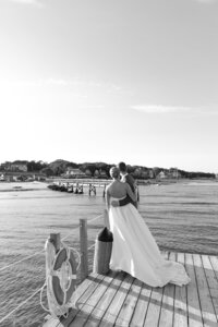 Bride and Groom embrace while standing on dock overlooking water.