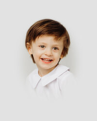 Toddler boy smiles for camera during heirloom portrait session in Raleigh NC studio