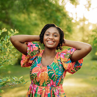 Senior girl in a floral dress posing by bright greenery in Chatom, Alabama.