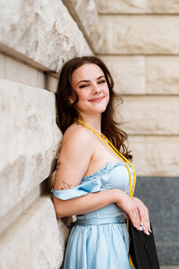 Belmont graduate wearing cord and leaning against the wall outside her college building