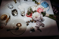 Late night photo of flowers, champagne, polaroid images and half-eaten wedding cake