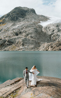 Portrait of bride and groom coming walking in Ipsoot Lake during their heli-elopement in British Columbia
