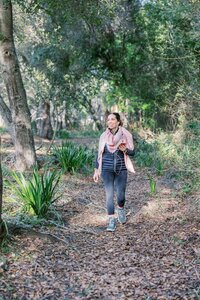 Woman walking through wooded area and taking a phone call on her headphones