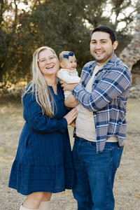 Parents smiling and holding their baby outdoors during golden hour, warm natural light family session photographed by Kaitlyn Dawn Photography, lifestyle family photographer.