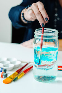 Local artist rinse her watercolor brush in a mason jar of blue water