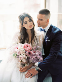 bride and groom sitting closely with a blush pink bouquet of peonies and ranunculus in soft natural light