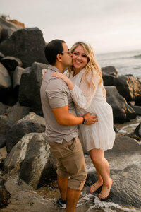 Couple embracing on coastal rocks at sunset during their Sunset Cliff portrait session