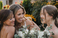 Mariée riant aux éclats entourée de ses demoiselles d'honneur, bouquets de fleurs blanches et verdure, décor floral en arrière-plan au Parc Maisonneuve, Montréal