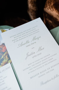 A wedding invitation printed on elegant ivory paper with soft green lettering, announcing the marriage of Ariella Mazza and Justin Max
