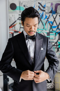 Groom looks down and buttons suit
