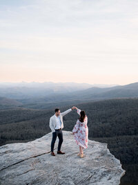 A wide-angle, intentional imagery capture of a couple dancing on a cliffside, highlighting the vast landscape of an East Coast mountain celebration on Blue Ridge Parkway.