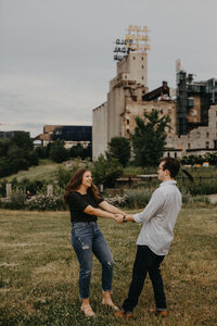engagement portrait with couple dancing in front of stone mill in minnesota