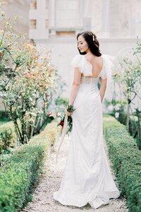 bride-white-dress-with-bouquet-flowers-stands-garden-rear-view