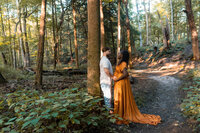 Expectant couple embracing on a forest path, wife in a rust orange gown, during a Cleveland maternity photography session