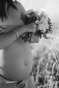 pregnant woman showing belly with flowers during maternity session in Christchurch