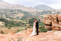 Romantic Colorado wedding portrait—bride and groom kissing on red rocks with rolling foothills behind at Willow Ridge Manor.