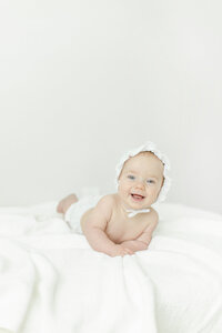 baby girl on belly holding head up wearing bonnett