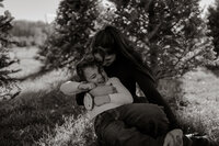 Maine family portrait of a mother cuddling and laughing with her son in her lap, capturing a joyful and heartfelt motherhood moment outdoors