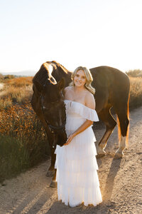 High school senior girl standing beside a horse in a golden field during sunset, outdoor senior photography by Kaitlyn Dawn Photography.