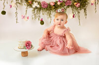 One year old baby in blush dress seated on white backdrop in New Bern studio