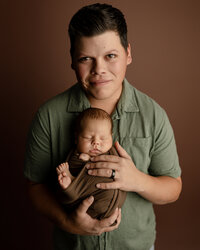 Father holding his sleeping newborn baby during a warm studio newborn family portrait session in Yucaipa by Kaitlyn Dawn Photography.