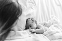 Newborn baby peacefully sleeping against mother’s chest during a black-and-white lifestyle newborn photography session with Nature’s Child Photography, tiny fingers curled gently against her skin beneath soft blankets and natural window light in St. Johns Florida.