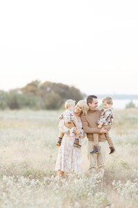 Beautiful family portrait of a mother and father holding their two young boys as they pose for family photos in the middle of an open field at a Dallas park.