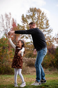 Father playfully holding his daughter's raised hand while walking through an autumn park during a Cleveland family photography session