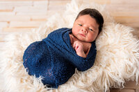 Newborn baby wrapped in blue fabric on soft neutral backdrop in New Bern studio