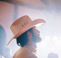 Groom in a cowboy hat looks toward the dance floor during an Asheville wedding reception, lights softly flaring behind him.