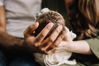 A curly haired newborn lies in her parents hands.