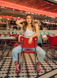 Senior portrait at Sunliner Diner in Gulf Shores, Alabama — sitting backward in a red diner chair,
holding her hair and facing the camera.