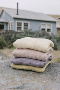 Stack of folded AW26 sweaters in cream, blush, lavender and chartreuse photographed on location