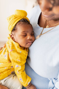 New mom in a blue dress holding and admiring her baby in a yellow outfit and bow