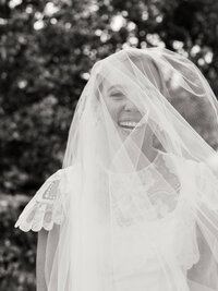 A close-up, joyful real moment of a bride laughing under her veil, preserving the atmosphere and emotion of a Charleston wedding morning.