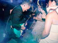 A high-energy shot of a live guitarist with colorful light trails, capturing the vibrant atmosphere of a luxury wedding weekend.