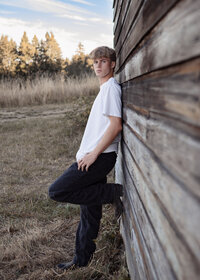 Sam Barlow high school senior boy leaning against the bat barn at Milo Mciver Park in Estacada Oregon for his senior portraits
