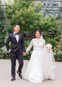 Elegant wedding portraits—bride in lace gown and groom in tux walking hand-in-hand outdoors