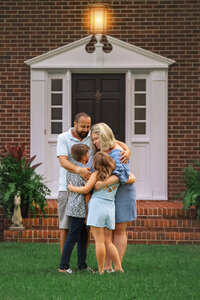 Parents hugging their two children in front of a brick home during a family session in New Bern