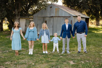 Large family standing together outdoors in front of a rustic barn, coordinated blue outfits and natural golden hour lighting captured by Kaitlyn Dawn Photography, extended family portrait photographer.