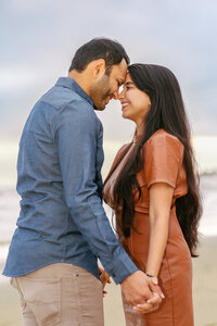 Couple sharing an intimate moment during a sunset photo session on the beach, captured in soft golden light.