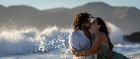 couple passionately kissing in the heavy surf as the waves crash against the rocks in the background