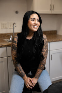 Woman with long dark hair and tattoos standing in a modern salon setting. Photograph by Yucaipa branding photographer Kaitlyn Dawn Photography.