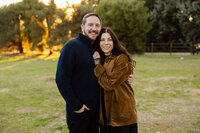 Couple embracing closely in a grassy park at sunset, warm golden hour portrait captured by Kaitlyn Dawn Photography, professional couples’ photographer.