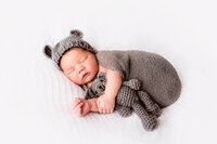 Sleeping newborn wrapped in gray knit with bear bonnet in New Bern photography studio