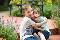 Two energetic boys in Palm Coast, burst into laughter while hugging on a brick patio during a carefree outdoor portrait session. - A portrait experience by Nature's Child Photography.