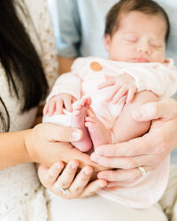 Close-up detail of newborn baby feet gently held in mom and dad’s hands during an in-home lifestyle newborn session.